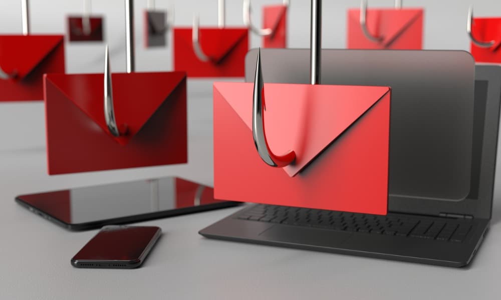 A concept image depicting cyber threats, featuring several red envelopes with hooks piercing through them, symbolizing phishing scams. The envelopes are placed over electronic devices including a laptop, tablet, and smartphone.