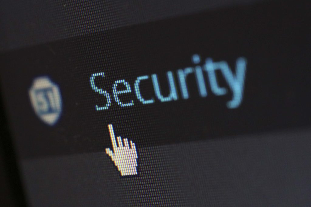 Close-up of a computer screen showing the word "Security" with a cursor in the shape of a pointing hand icon hovering over it. The background is dark, emphasizing the blue and white text and icon.