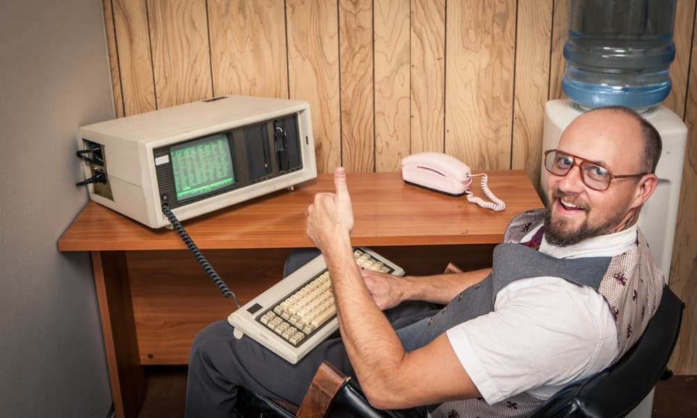 Outdated computer equipment and telephone with a nerdy-looking guy wearing outdated clothing.