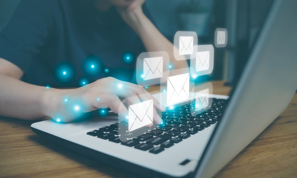 A person typing on a laptop keyboard with multiple email icons floating above, symbolizing sending or receiving emails. The background is slightly blurred, emphasizing the focus on the hands and icons. Blue light effects add a digital, futuristic feel.